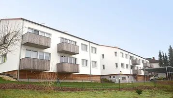 Modernes Mehrfamilienhaus mit weißen Fassaden, Holzverkleidungen und Balkonen in grüner Umgebung.
