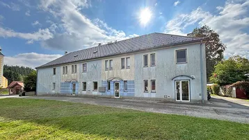 Gebäudeansicht von vorne mit hellblauer Fassade, grüner Wiese und sonnigem Himmel.