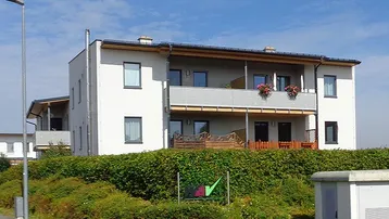 Modernes Mehrfamilienhaus mit Balkonen und gepflegter Hecke in sonniger Lage.