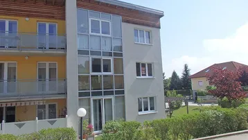 Moderne Wohnhausfassade mit großen Glasflächen, Balkonen und gepflegter Grünanlage.