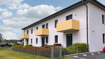 Moderne Wohnanlage mit weißer Fassade, gelben Balkonen und grüner Umgebung unter blauem Himmel.