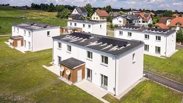 Luftaufnahme von modernen Reihenhäusern mit Photovoltaikanlagen auf den Flachdächern in grüner Landschaft.