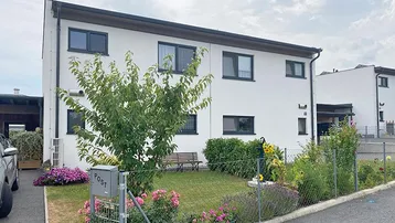 Modernes Einfamilienhaus mit weißer Fassade, dunklen Fenstern und gepflegtem Vorgarten.