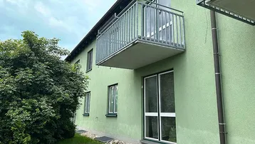Grüne Fassade eines Mehrfamilienhauses mit Balkon und großen Fenstern.