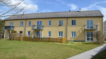 Mehrfamilienhaus mit gelber Fassade, Balkonen und einem gepflegten Rasenbereich davor.