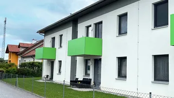 Modernes Mehrfamilienhaus mit weißer Fassade und leuchtend grünen Balkonen.