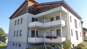 Mehrfamilienhaus mit mehreren Balkonen und Holzverkleidung unter dem Dach.