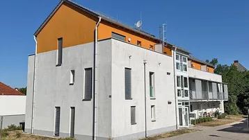 Modernes Mehrfamilienhaus mit weißer und oranger Fassade unter blauem Himmel.