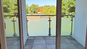 Balkon mit Fliesenboden und Glasbrüstung, bietet einen Blick ins Grüne.
