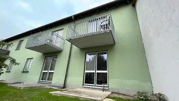 Grüne Fassade eines Mehrfamilienhauses mit zwei Balkonen und Zugang zum Gartenbereich.