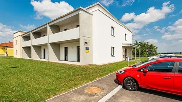 Modernes Mehrfamilienhaus mit weißer Fassade, Balkonen und gepflegten Grünflächen.