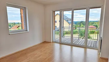 Geräumiges Wohnzimmer mit Laminatboden, großen Fenstern und Zugang zum Balkon mit Weitblick.