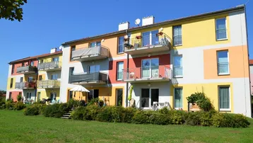 Farbenfrohe Fassade eines modernen Mehrfamilienhauses mit Balkonen, Terrassen und Grünflächen.
