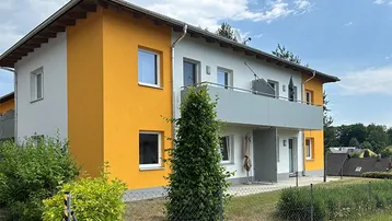 Modernes Mehrfamilienhaus mit weißer und orangefarbener Fassade sowie einem Balkon.