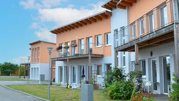 Moderne Reihenhäuser mit orangefarbenen Fassaden, Balkonen und kleinen Gärten unter blauem Himmel.