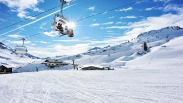 Sonniger Skitag in den Bergen mit Skilift und verschneiten Pisten unter blauem Himmel.