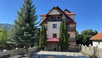 Großes Gebäude mit traditioneller Architektur, umgeben von Bäumen und einem gepflasterten Vorplatz.