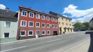 Mehrere Gebäude entlang einer Straße unter blauem Himmel mit Wolken.