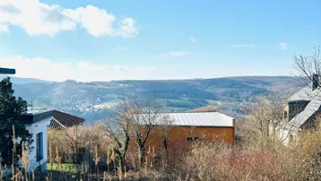 Weitläufiger Blick über die hügelige Landschaft mit vereinzelten Häusern unter blauem Himmel.
