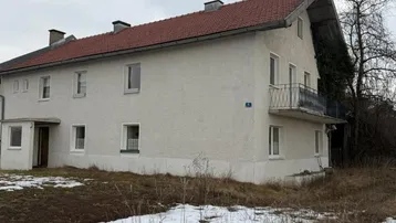 Einfamilienhaus mit heller Fassade, Satteldach und kleinem Balkon in ländlicher Umgebung mit Schneeresten.