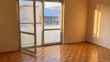 Helles Wohnzimmer mit Parkettboden und Zugang zu einem Balkon oder einer Terrasse.