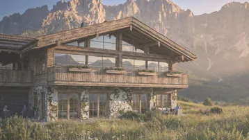 Traditionelles Holzchalet mit Steinfassade und großen Fenstern vor einer beeindruckenden Bergkulisse.