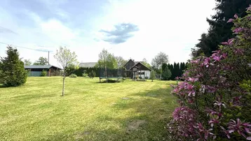 Großer, gepflegter Garten mit Rasenfläche, Trampolin und blühenden Sträuchern, umgeben von Bäumen.