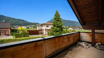 Balkon mit Holzboden und weitem Blick auf die grüne Berglandschaft und Nachbarhäuser.