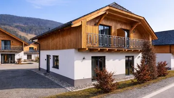 Modernes Holzhaus mit weißer Fassade und Balkon in alpiner Umgebung.