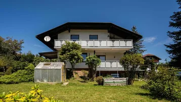 Großzügiger Gartenbereich mit Gewächshaus und Blick auf die Hausfassade mit Balkonen.