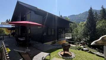 Sonniger Gartenbereich mit Liegestühlen, Feuerstelle und Blick auf die umliegenden Berge.