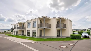 Modernes Mehrfamilienhaus mit Balkonen und gepflegter Außenanlage unter bewölktem Himmel.