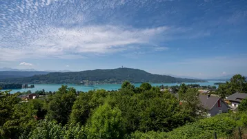 Panoramablick auf den See und die umliegende grüne Landschaft unter blauem Himmel.