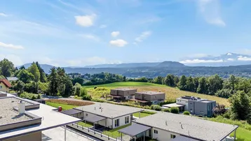 Weitläufige Aussicht über die umliegende Landschaft mit weiteren modernen Wohnhäusern und Bergen im Hintergrund.