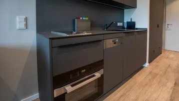Moderne, eingebaute Küchenzeile in elegantem Schwarz mit integrierten Geräten und Holzfußboden.