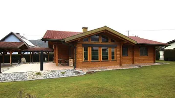 Blockhaus mit rotem Ziegeldach, großen Fenstern und gepflegtem Rasen.