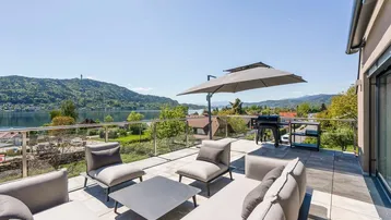 Große Sonnenterrasse mit bequemen Loungemöbeln, Grillbereich und weitem Blick auf den See und die Berge.
