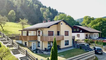 Freistehendes Haus mit beiger Fassade, Balkonen und gepflegtem Garten in ländlicher Umgebung.