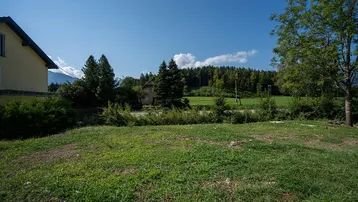 Weitläufige Rasenfläche mit Bäumen und Blick auf die bewaldete Hügellandschaft unter blauem Himmel.