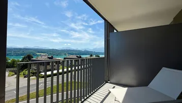 Geräumiger Balkon mit bequemer Liege und atemberaubendem Blick auf den See und die umliegenden Berge.