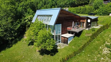 Modernes Haus mit Holzfassade und Metallverkleidung, eingebettet in eine grüne Hanglage.