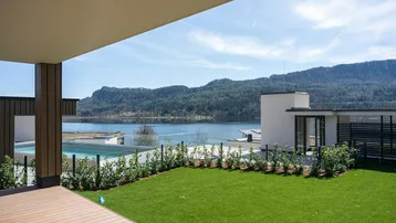 Geräumige Holzterrasse mit Blick auf den See, umgeben von Rasenfläche und einem Pool.