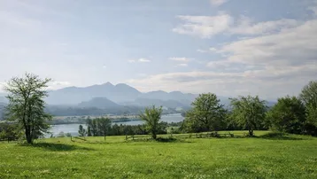 Weitläufige grüne Landschaft mit einem See und majestätischen Bergen im Hintergrund unter einem klaren Himmel.