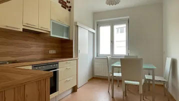 Helle Küche mit beigen Schränken, Holzakzenten und einem Essbereich am Fenster.