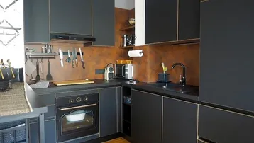 Moderne Küche mit schwarzen Schränken, dunkler Arbeitsplatte und rostfarbener Rückwand.