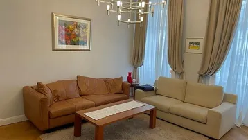 Helles Wohnzimmer mit bequemen Sofas, Holztisch und elegantem Kronleuchter unter hohen Decken.
