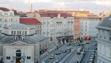 Panoramablick über eine belebte Stadtstraße mit historischen Gebäuden und Straßenbahnverkehr.