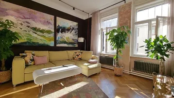Helles Wohnzimmer mit bequemer Couch, Kunstwerken an der Wand und großen Fenstern.
