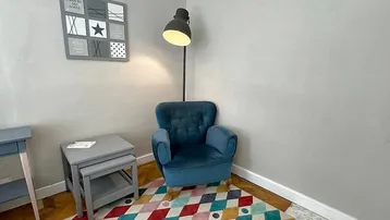 Gemütliche Leseecke mit blauem Sessel, Stehlampe und farbenfrohem Teppich auf Parkettboden.