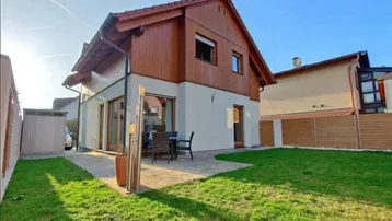 Modernes Einfamilienhaus mit Holzfassade, gepflegtem Rasen und einer gemütlichen Terrasse für Mahlzeiten im Freien.